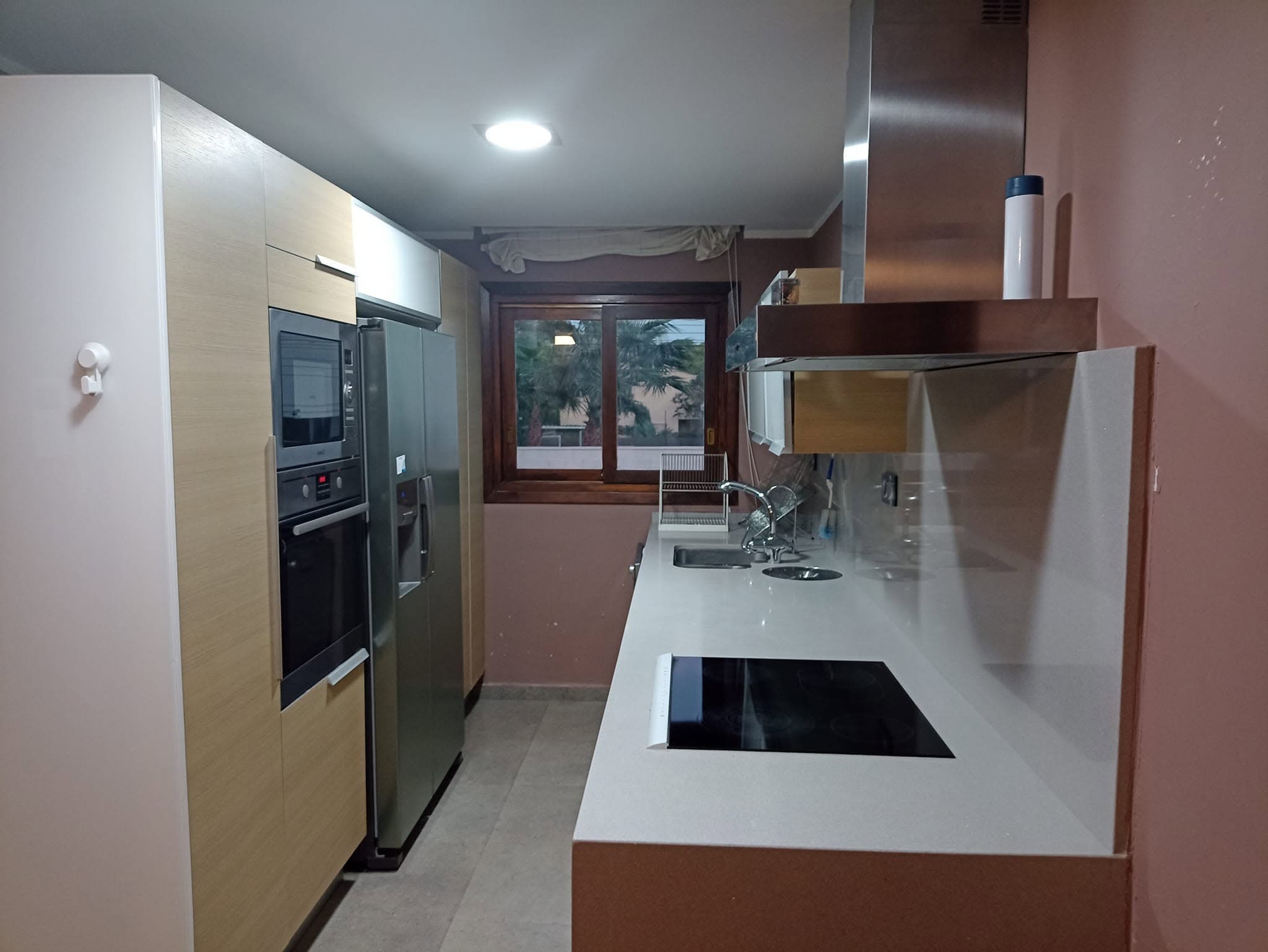 Cocina alargada con encimera blanca, placa de inducción y electrodomésticos, recién limpia