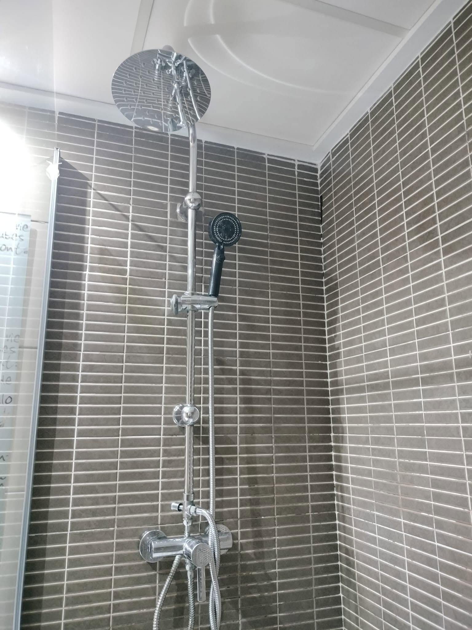 Ducha con azulejos grises y columna de ducha cromada, limpia y brillante